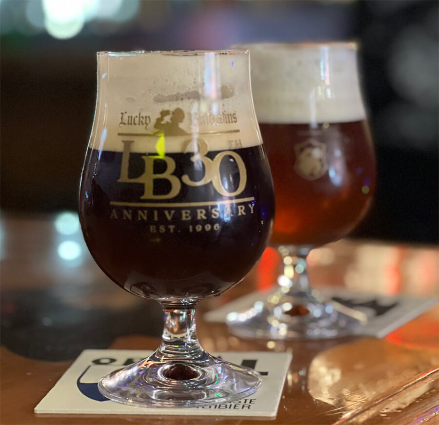 two lucky baldwins 30th anniversary glasses, one with a dark beer, and the other with an amber beer. sitting on a bar top.